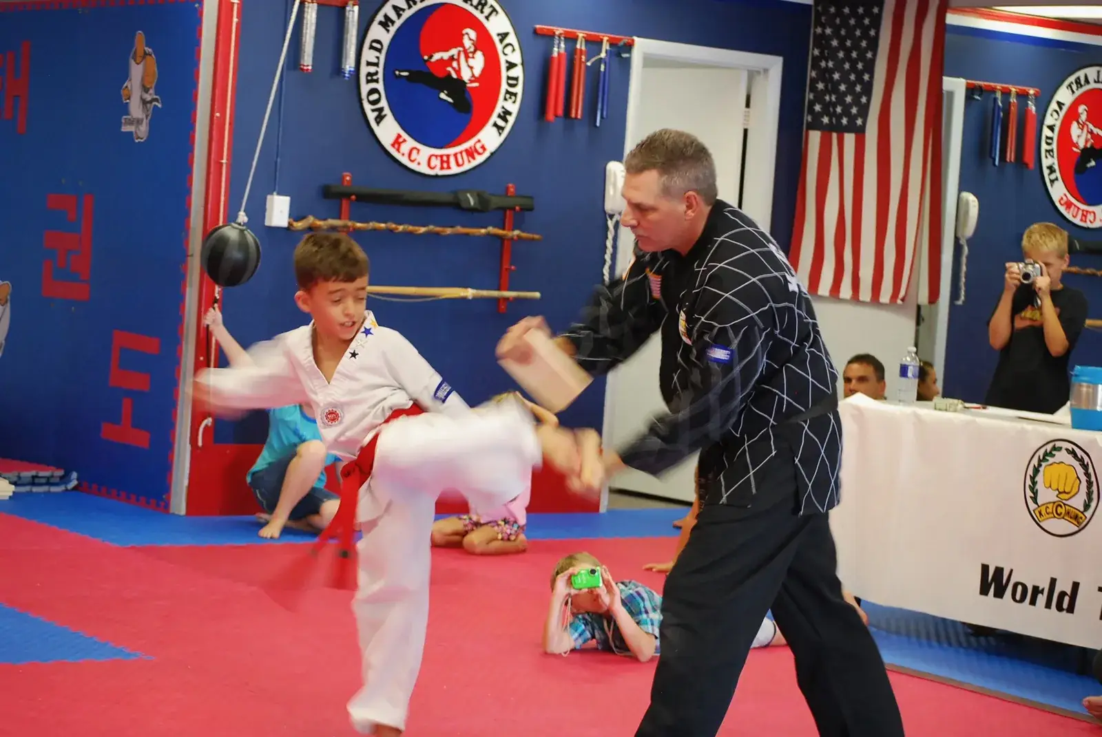 Child in a red belt kicking a target held by an instructor